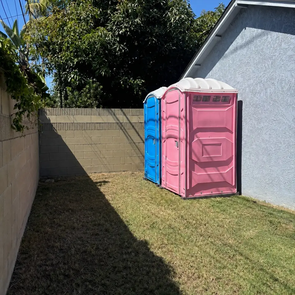 Two porta potties placed beside a home for a backyard party