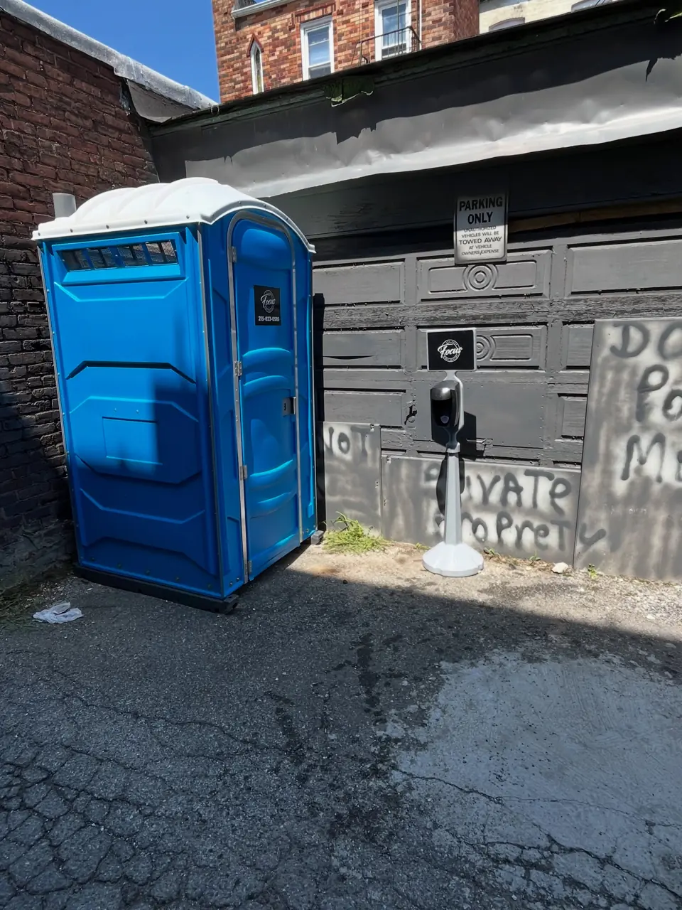 Blue porta potty placed at a job site beside a brick building