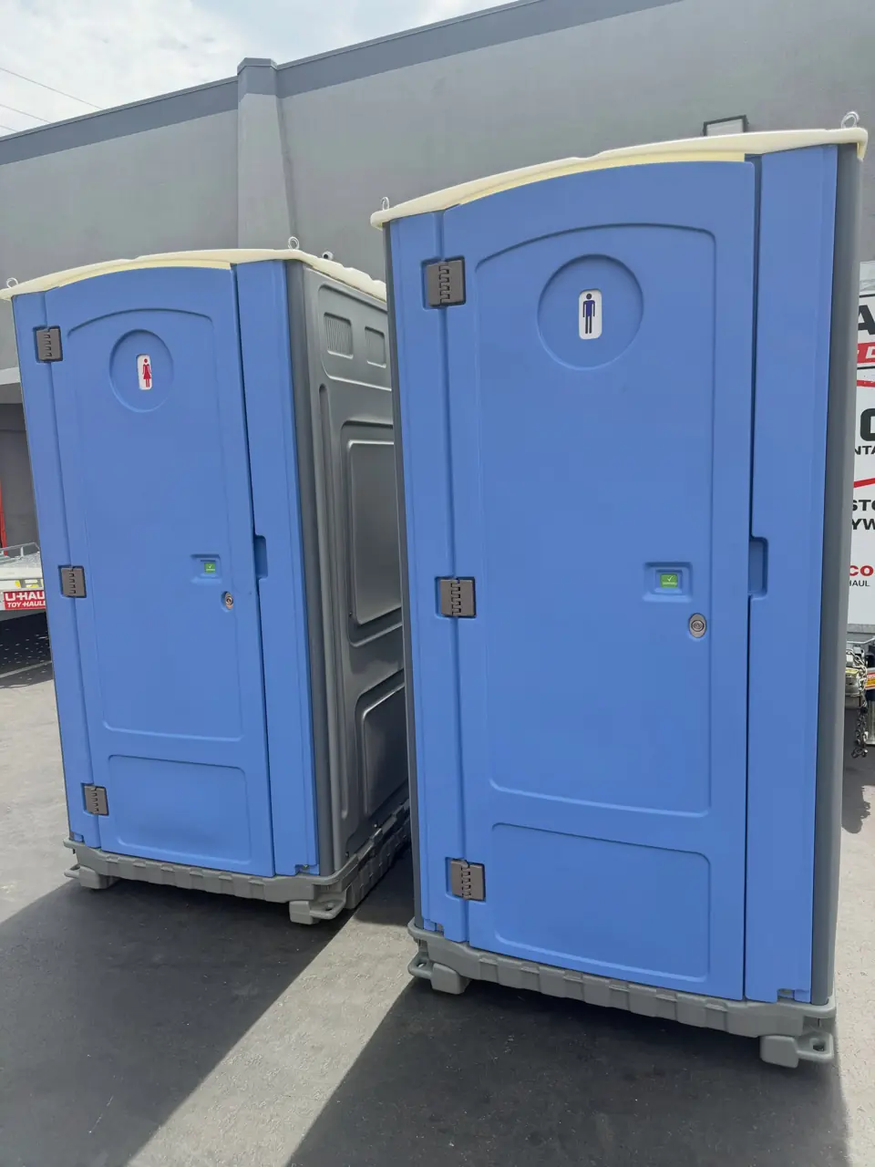 Two blue porta potties ready on a paved lot
